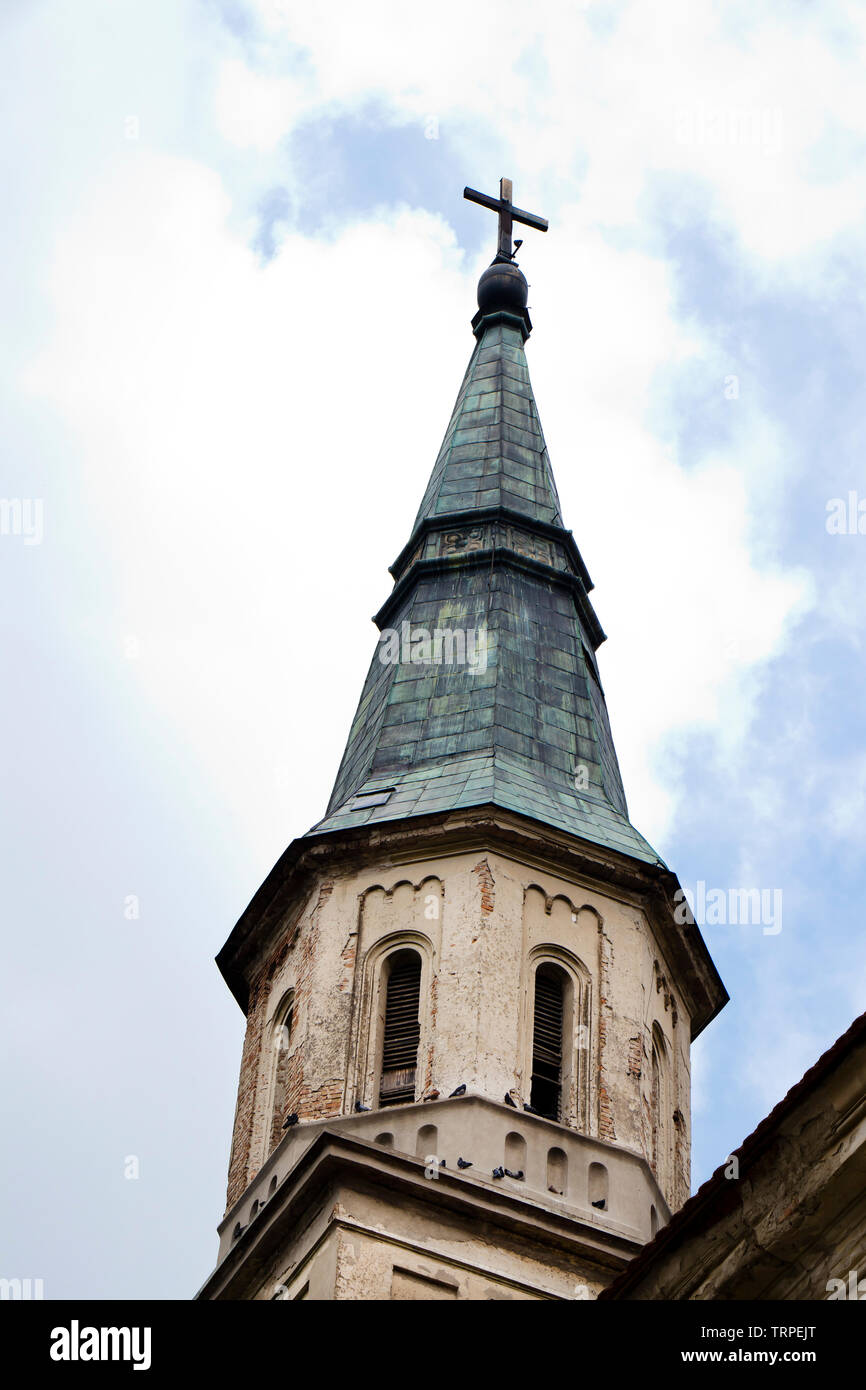 Tower with pointed cooper green roof of an old weathered catholic church in Ecka, Serbia, close up against cloudy sky Stock Photo