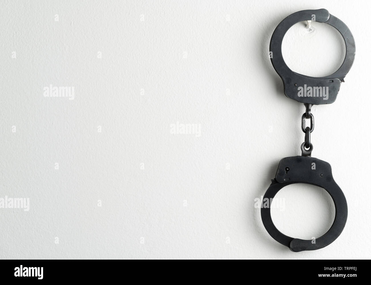 Police handcuffs on a white painted wall. Potential copy space to the left of handcuffs. Stock Photo