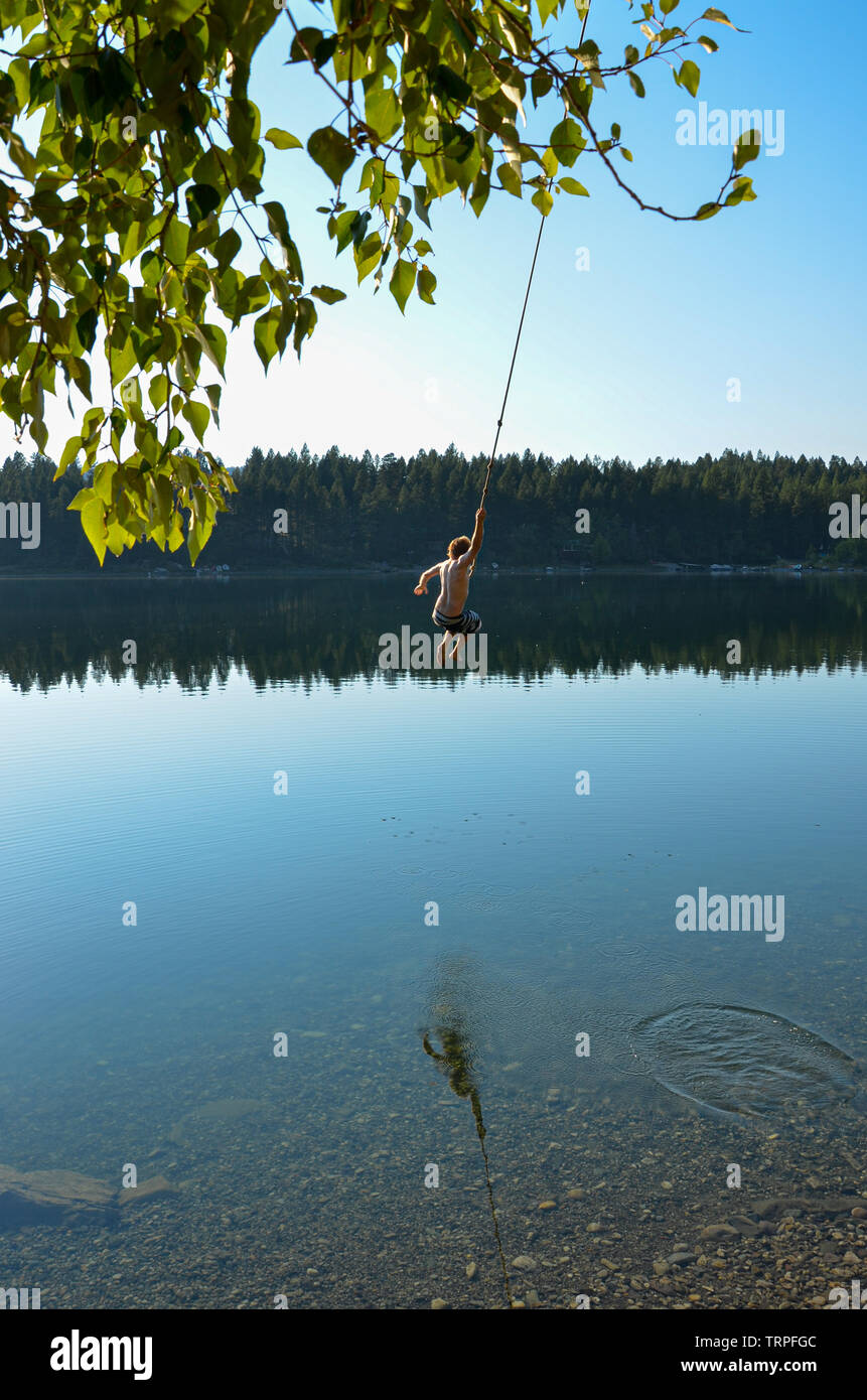 man swinging on a rope swing into a lake in Canada Stock Photo