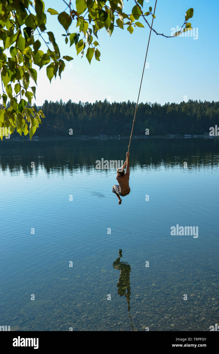 a guy swinging on a rope swing into a lake in Canada Stock Photo