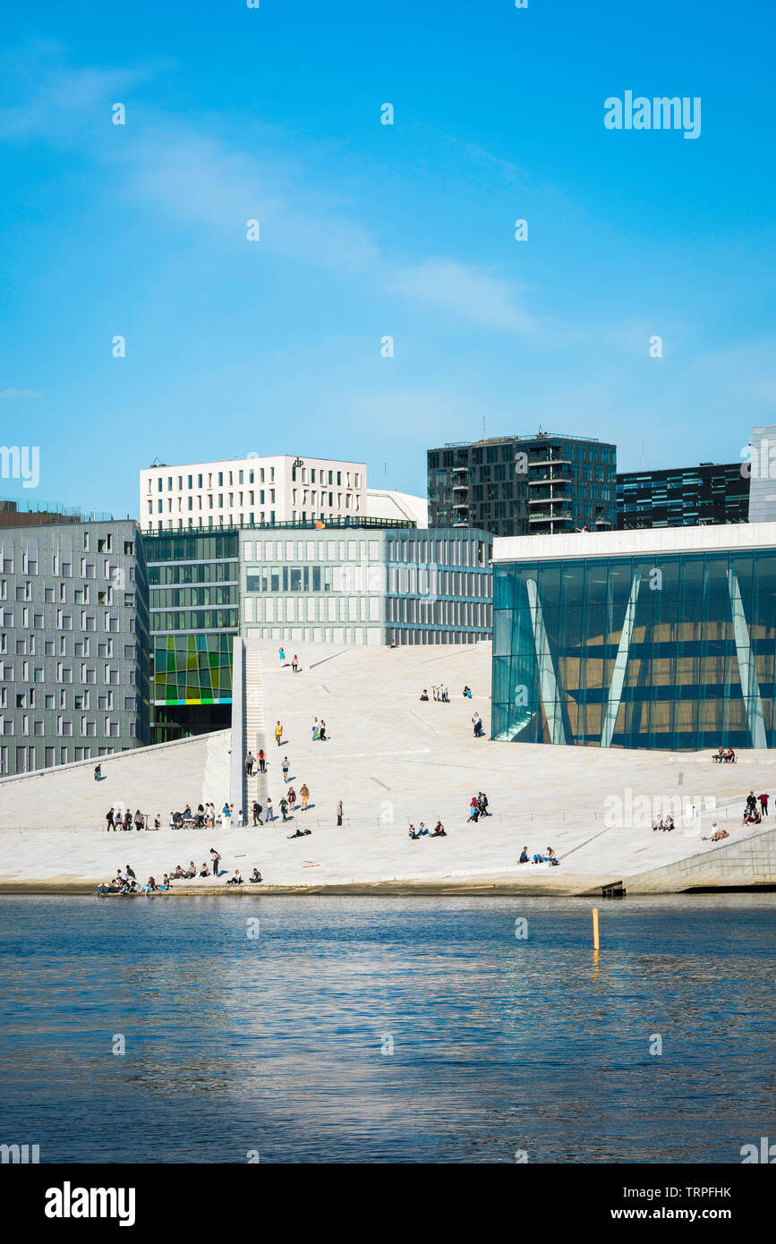 Oslo Opera House, view across Oslofjord of people on the vast access ramp leading to the roof of the Oslo Opera House, with Barcode Buildings beyond. Stock Photo