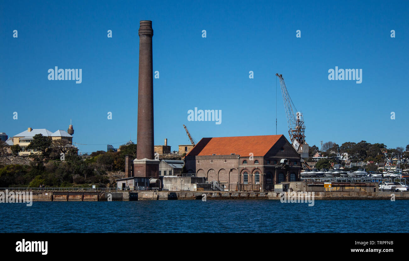 Factory brick smoke stack at historic dockyard and boat storage with crane against blue sky set on Cockatoo Island Sydney Harbour Australia Stock Photo