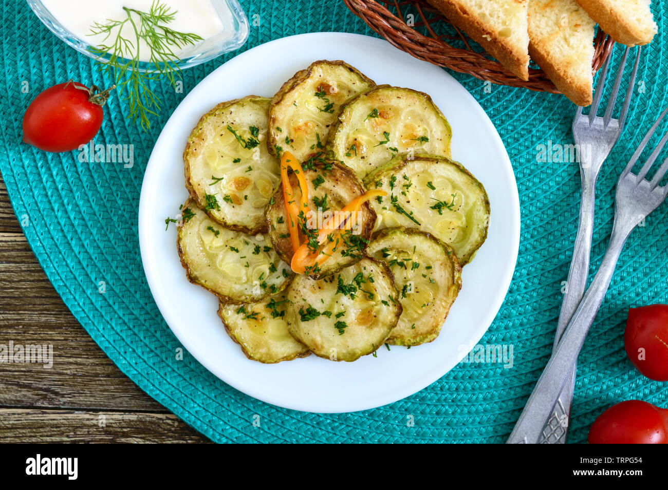 Tasty fried zucchini slices on a plate with sauce on a wooden table. Picnic snack. Rustic style. Top view, flat lay. Stock Photo