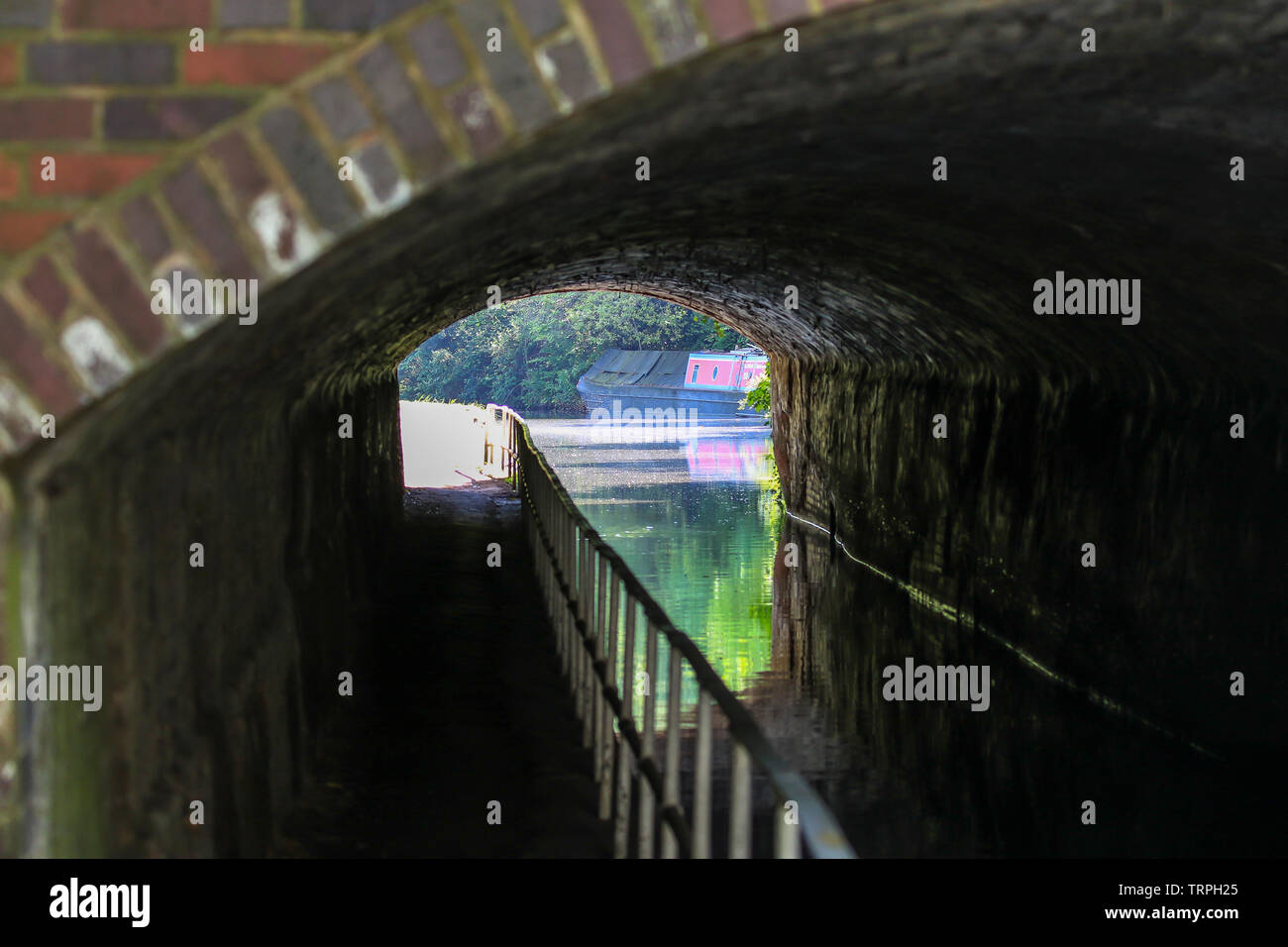 Landscape view looking through a dark, UK canal tunnel on bright sunny day. Detailed tunnel brickwork interior & outside sun reflected in canal water. Stock Photo