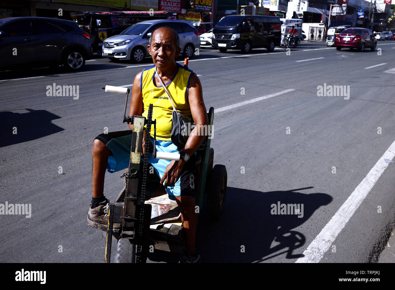 ANTIPOLO CITY, PHILIPPINES – JUNE 7, 2019: A person with disability peddles candies and cigarettes on his improvised wheelchair at a busy street. Stock Photo