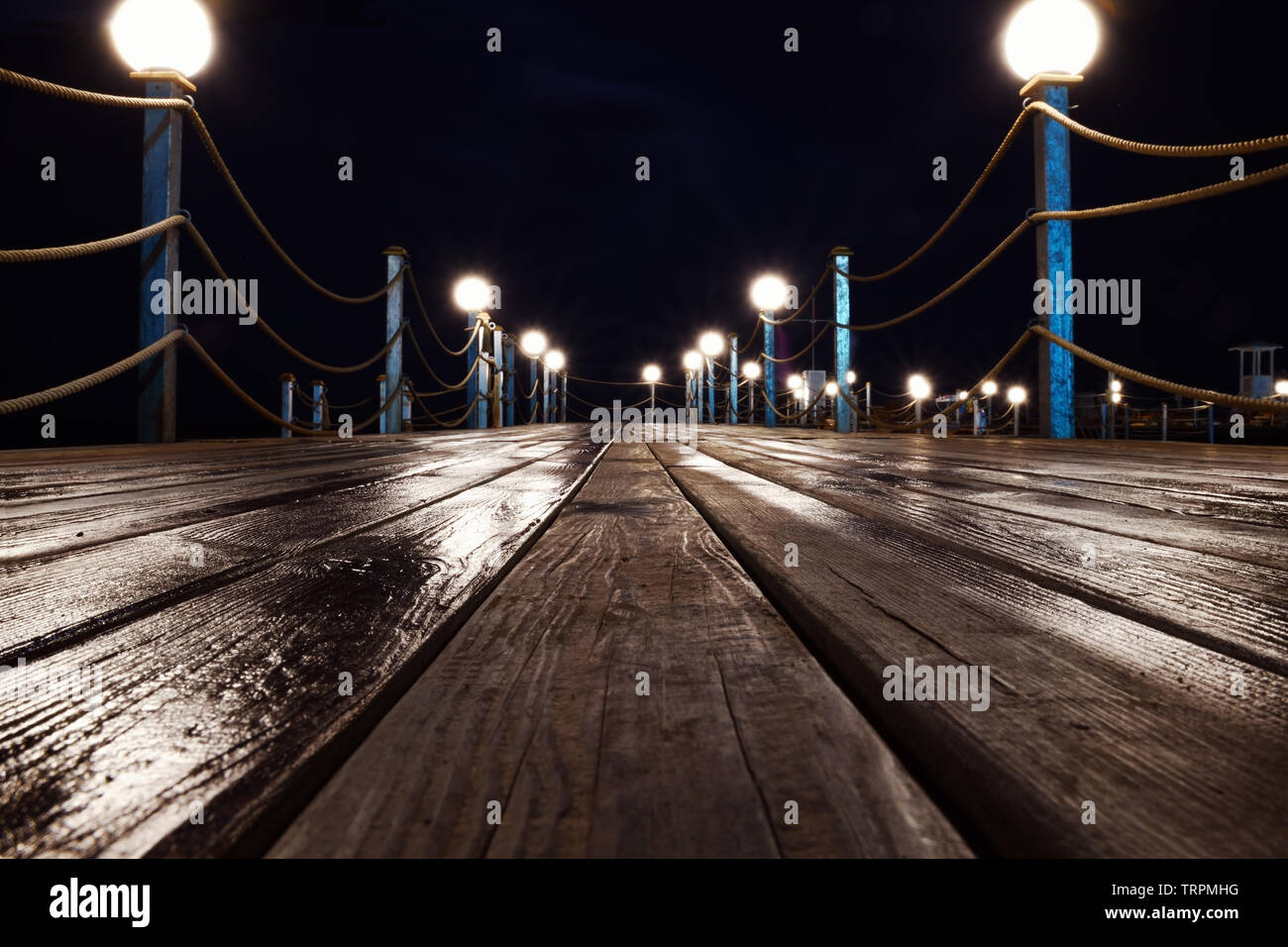 Wet wooden path with lights leads to the sea night. Concept background. Stock Photo