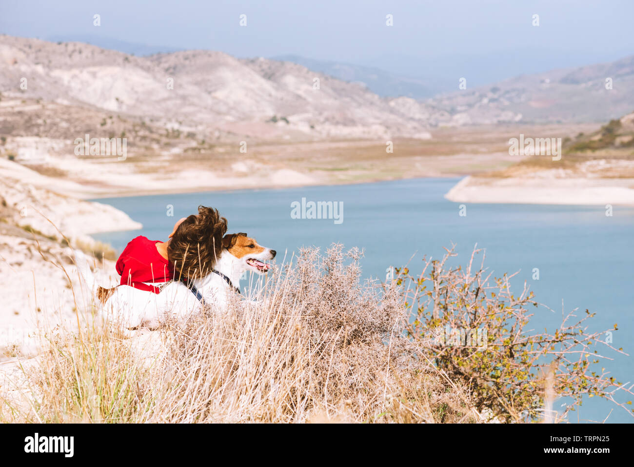 Travel, family and domestic life concept - kid and his pet dog relaxing at top of mountain looking at beautiful valley view Stock Photo