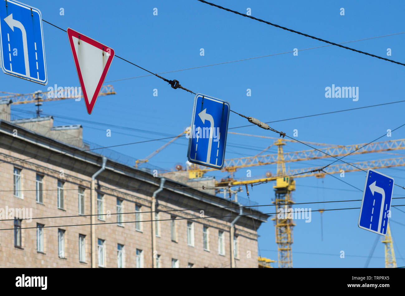 Road signs "turn left" and "give way" in the background construction cranes and blue sky Stock Photo