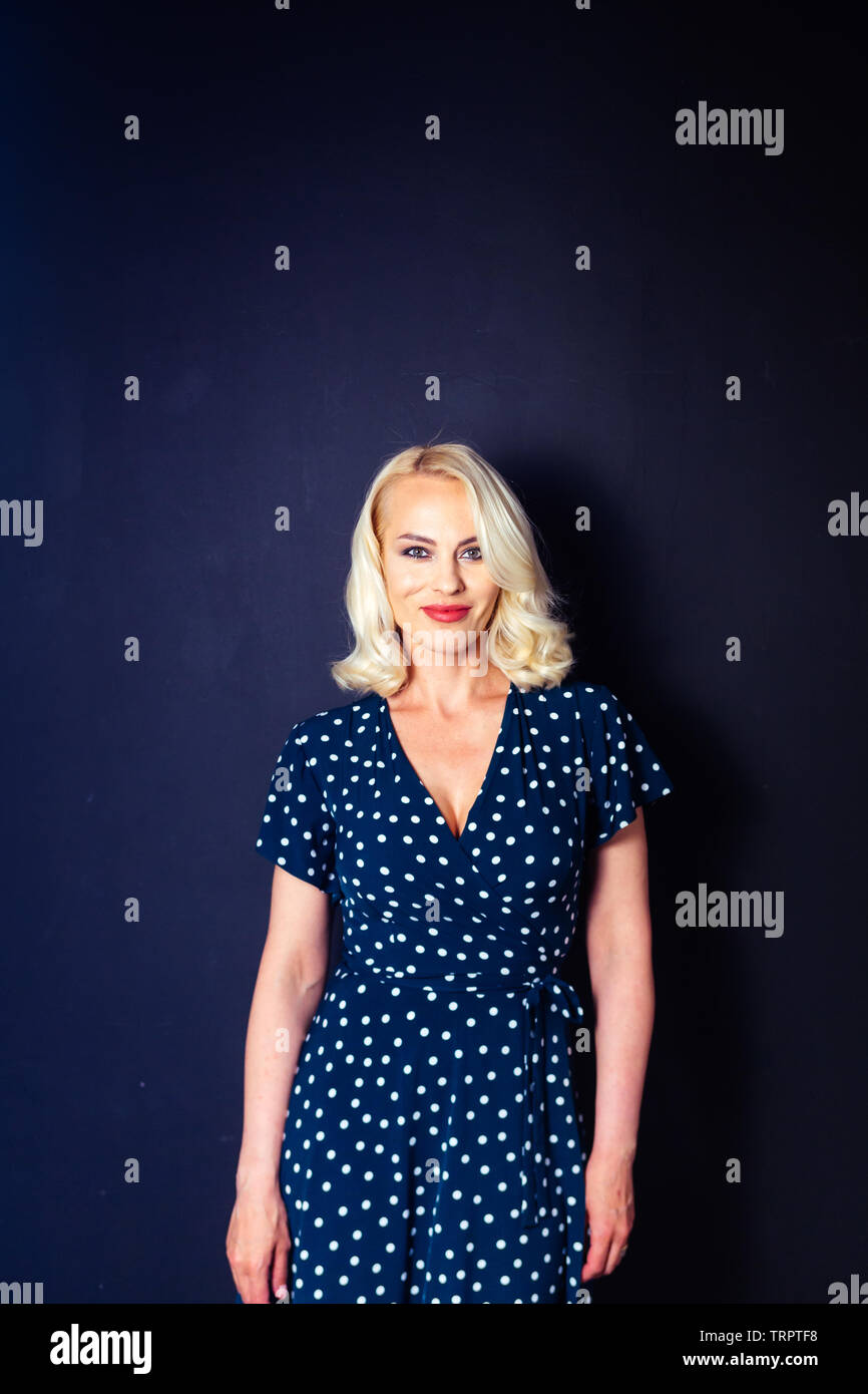 Studio portrait of beautiful blonde woman in a dark blue dress against ...