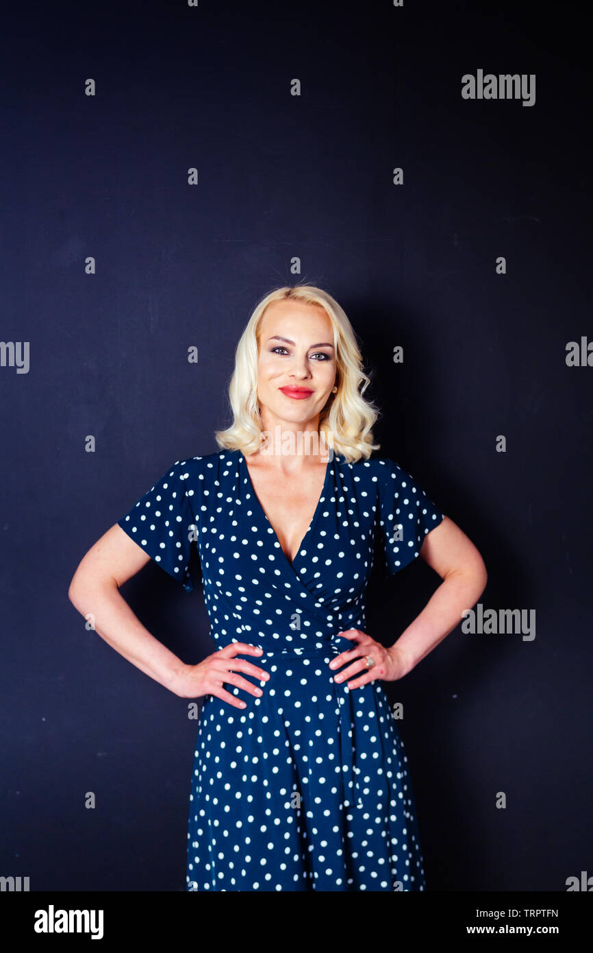 Studio portrait of beautiful blonde woman in a dark blue dress against ...