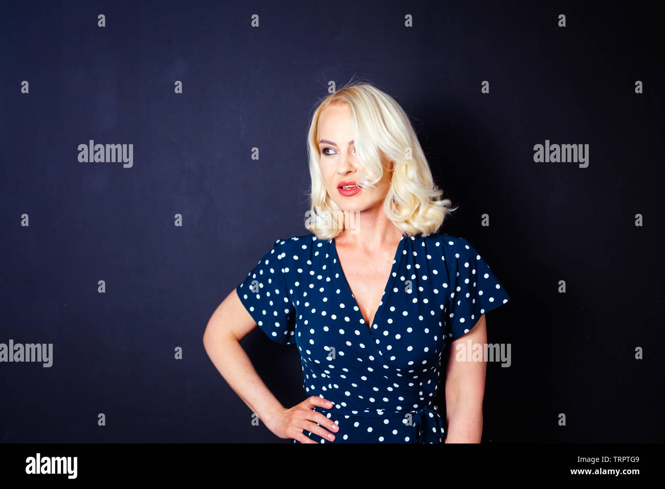 Studio portrait of beautiful blonde woman in a dark blue dress against ...
