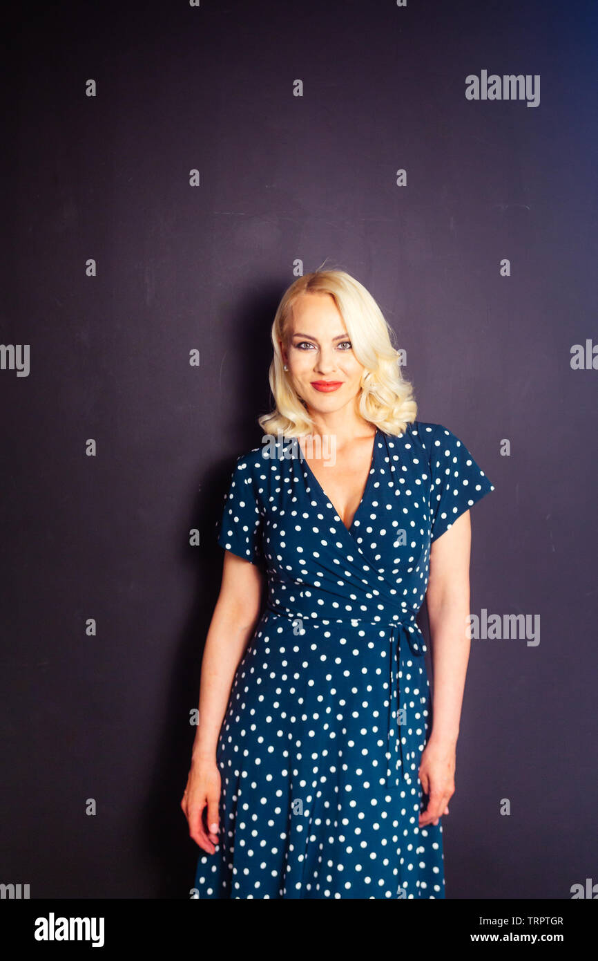 Studio portrait of beautiful blonde woman in a dark blue dress against ...