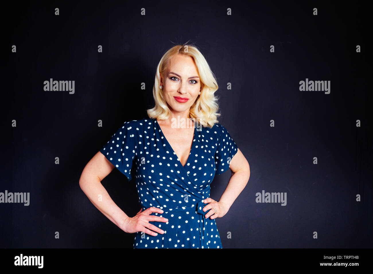 Studio portrait of beautiful blonde woman in a dark blue dress against black plain background Stock Photo