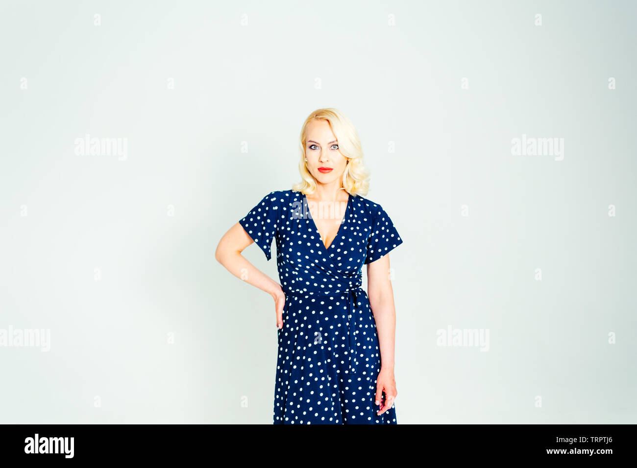 Studio portrait of beautiful blonde woman in a dark blue dress against white plain background Stock Photo