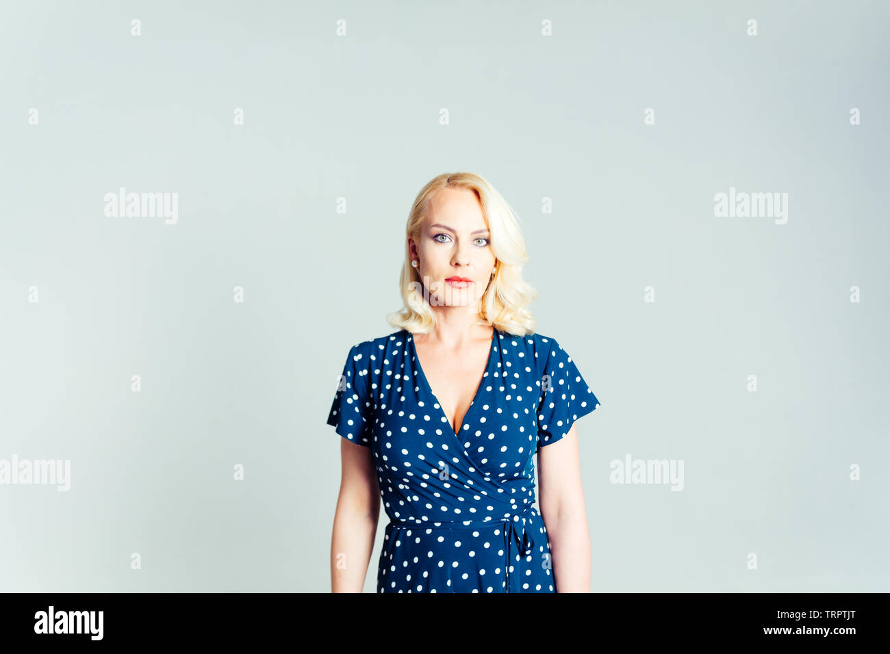 Studio portrait of beautiful blonde woman in a dark blue dress against ...
