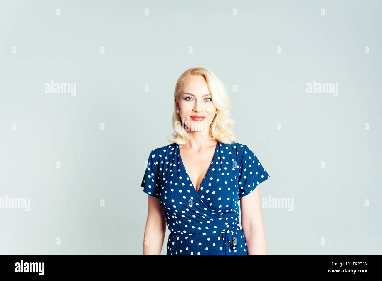 Studio portrait of beautiful blonde woman in a dark blue dress against ...