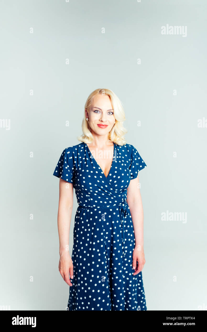 Studio portrait of beautiful blonde woman in a dark blue dress against ...