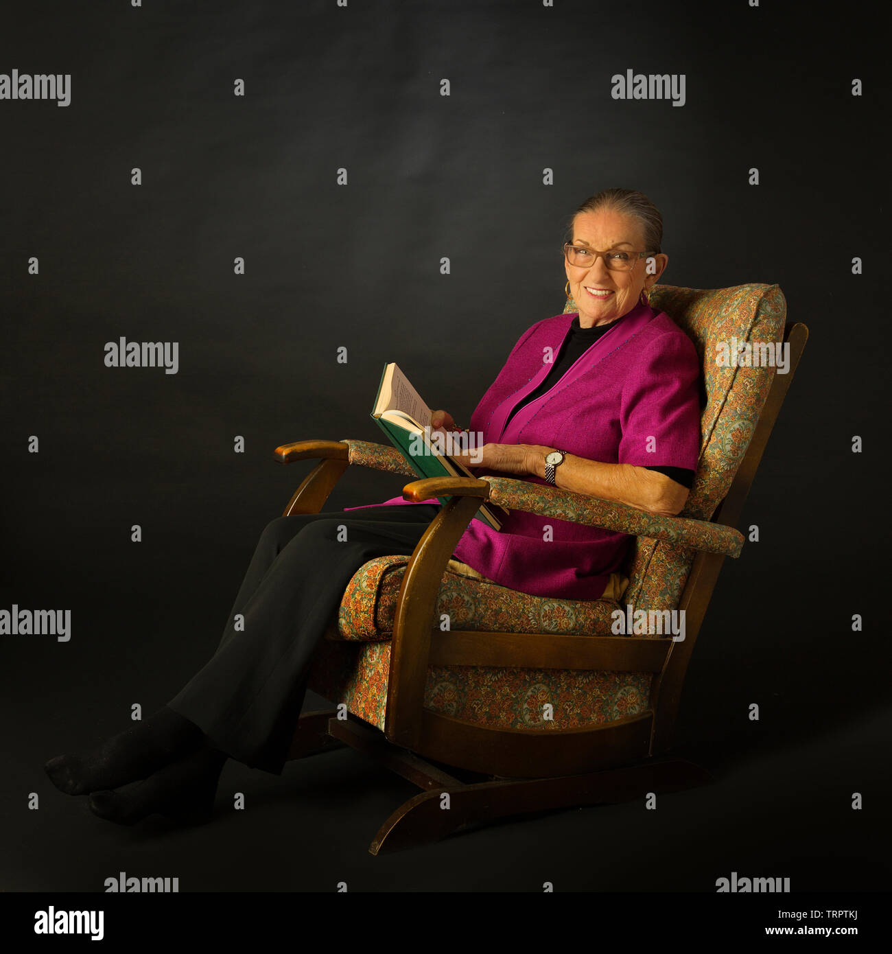 An octogenarian lady sitting in a rocking chair with a book Stock Photo