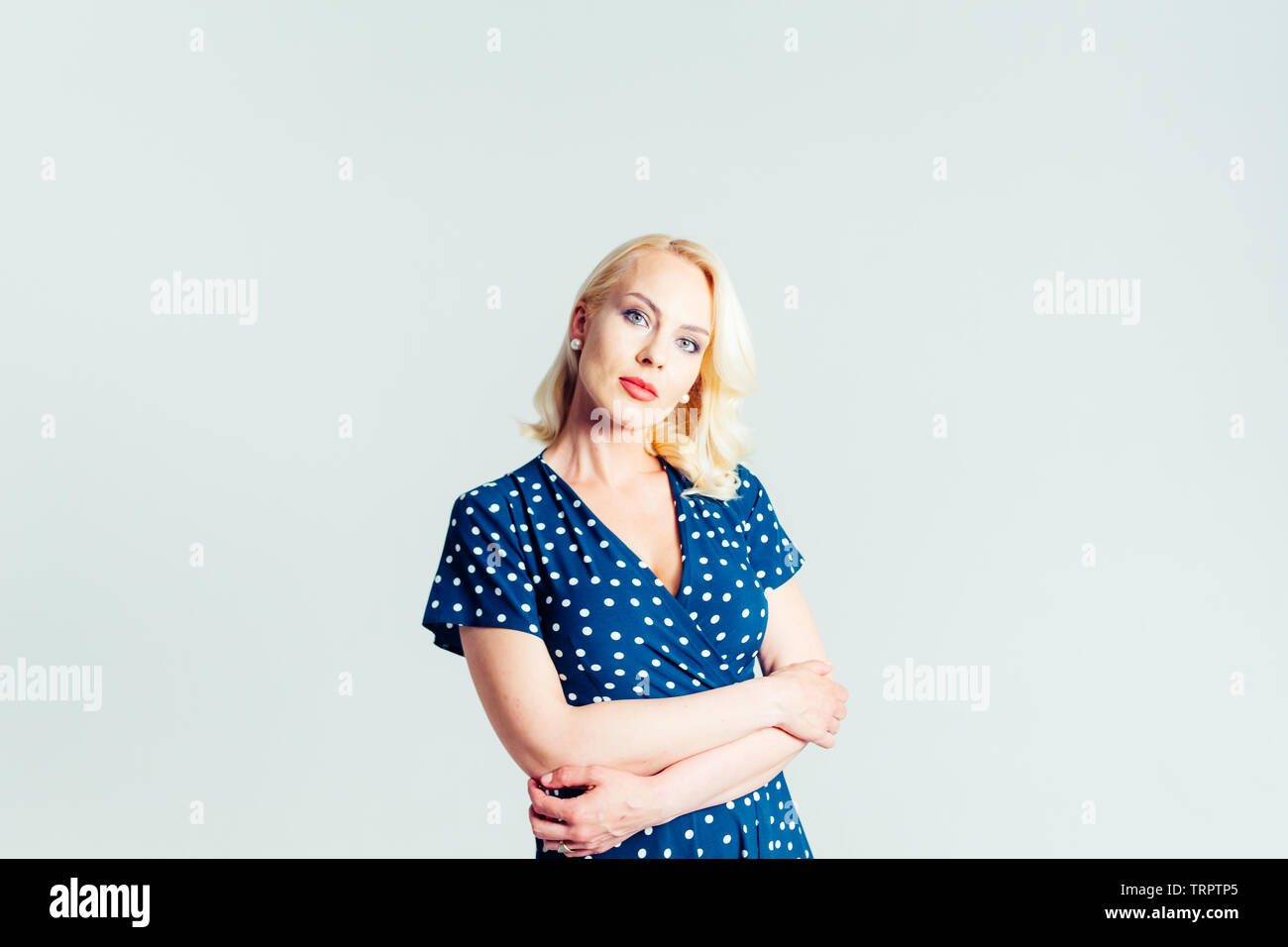 Studio portrait of beautiful blonde woman in a dark blue dress against ...
