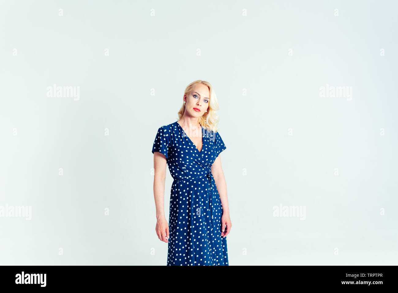 Studio portrait of beautiful blonde woman in a dark blue dress against ...