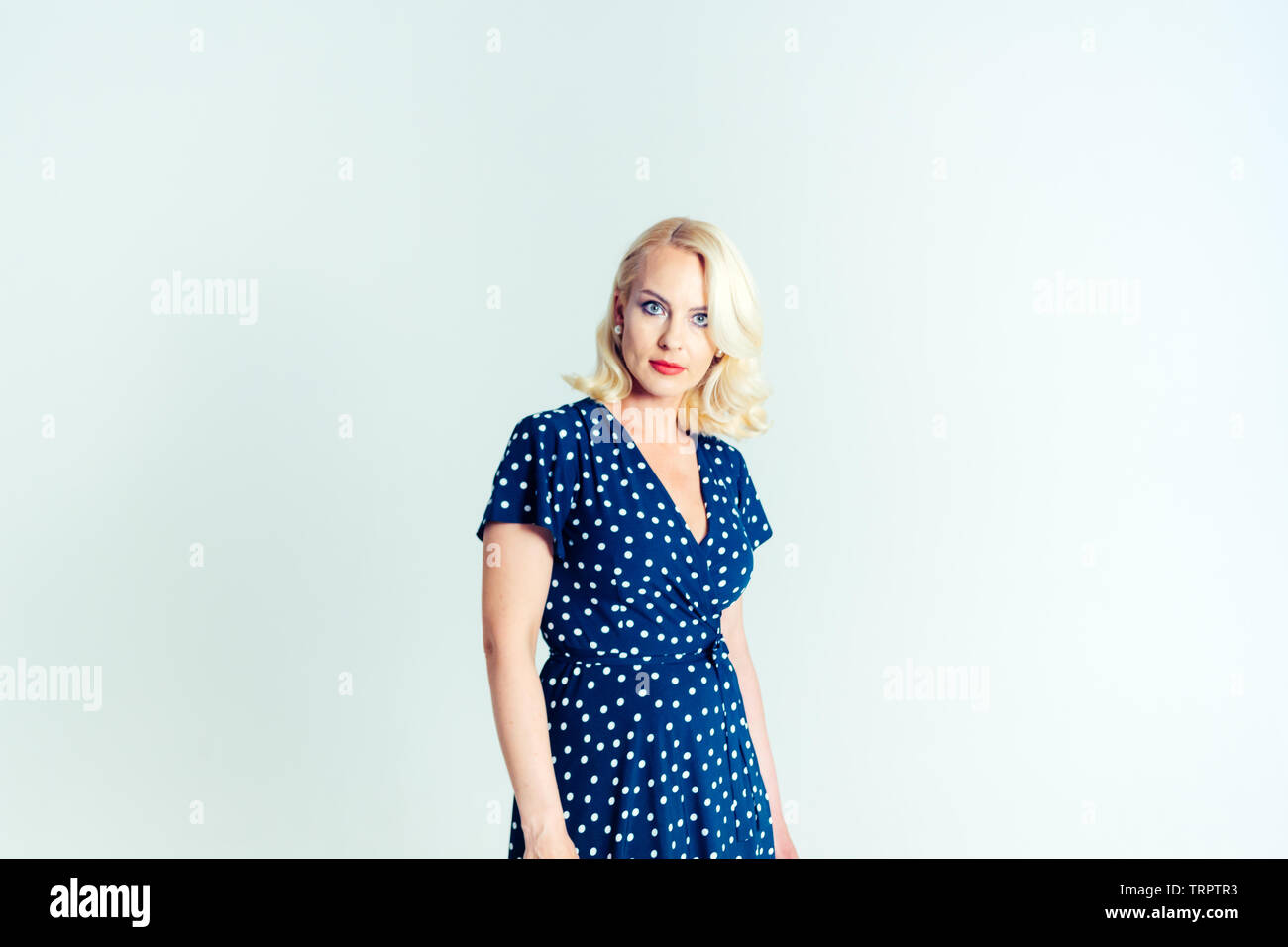 Studio portrait of beautiful blonde woman in a dark blue dress against ...