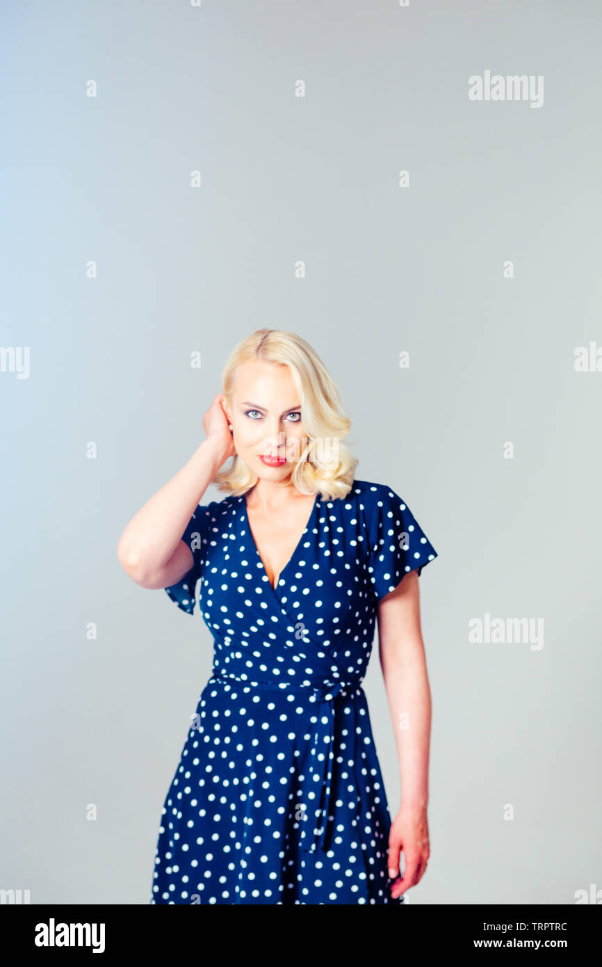 Studio portrait of beautiful blonde woman in a dark blue dress against ...