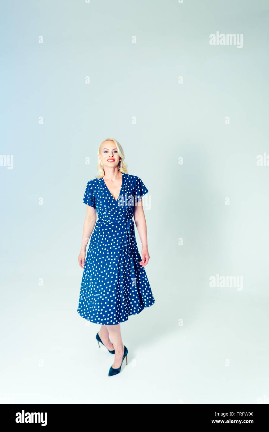 Studio portrait of beautiful blonde woman in a dark blue dress against ...