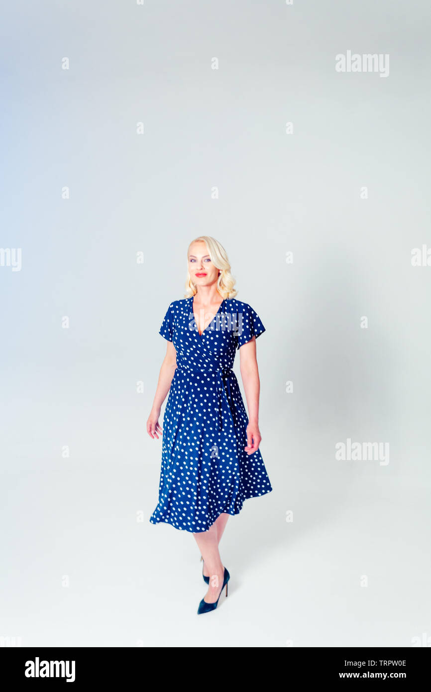 Studio portrait of beautiful blonde woman in a dark blue dress against white plain background Stock Photo