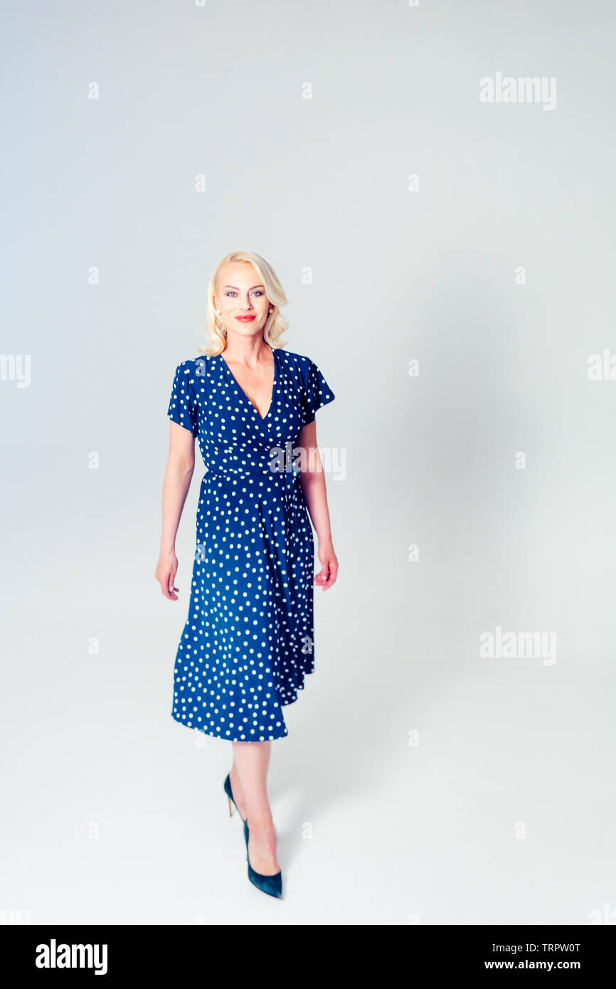 Studio portrait of beautiful blonde woman in a dark blue dress against ...