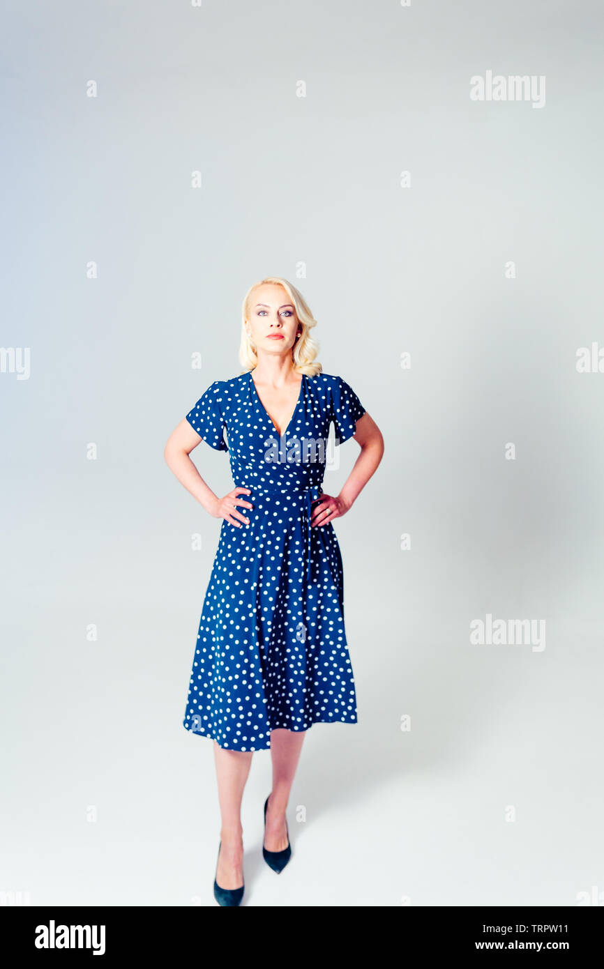 Studio portrait of beautiful blonde woman in a dark blue dress against ...