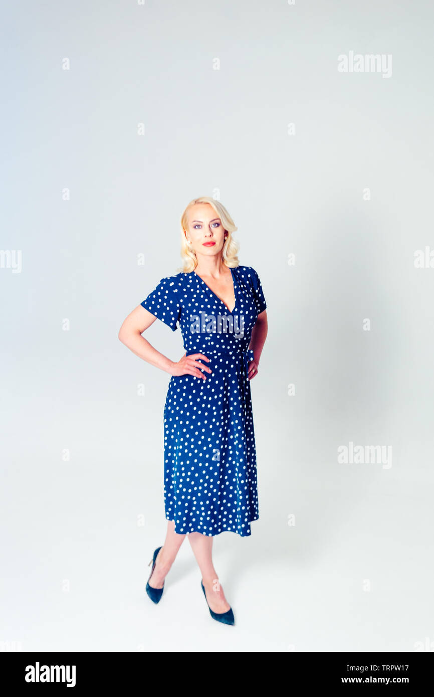 Studio portrait of beautiful blonde woman in a dark blue dress against ...