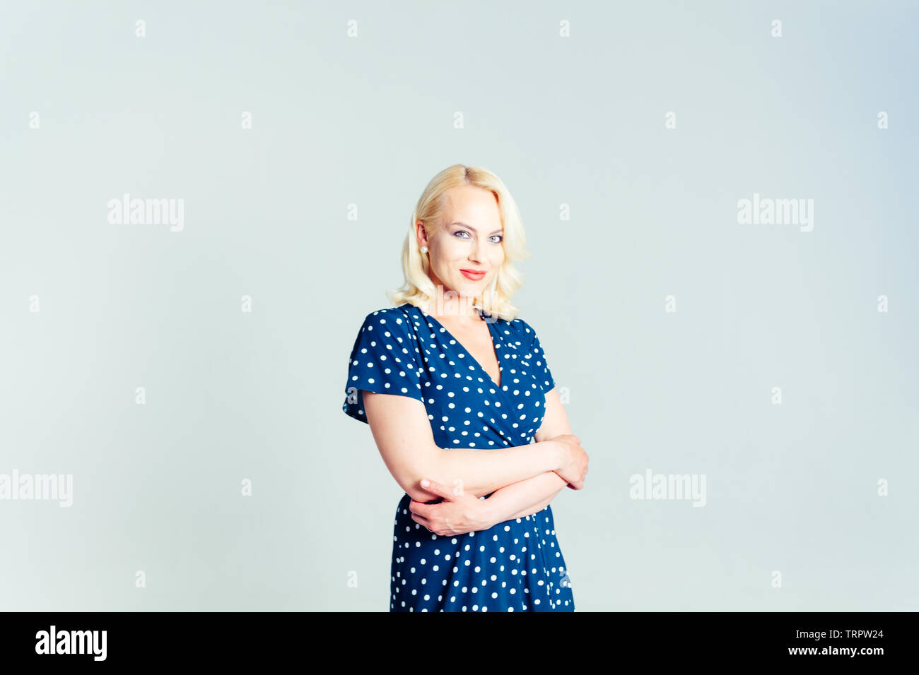 Studio portrait of beautiful blonde woman in a dark blue dress against ...