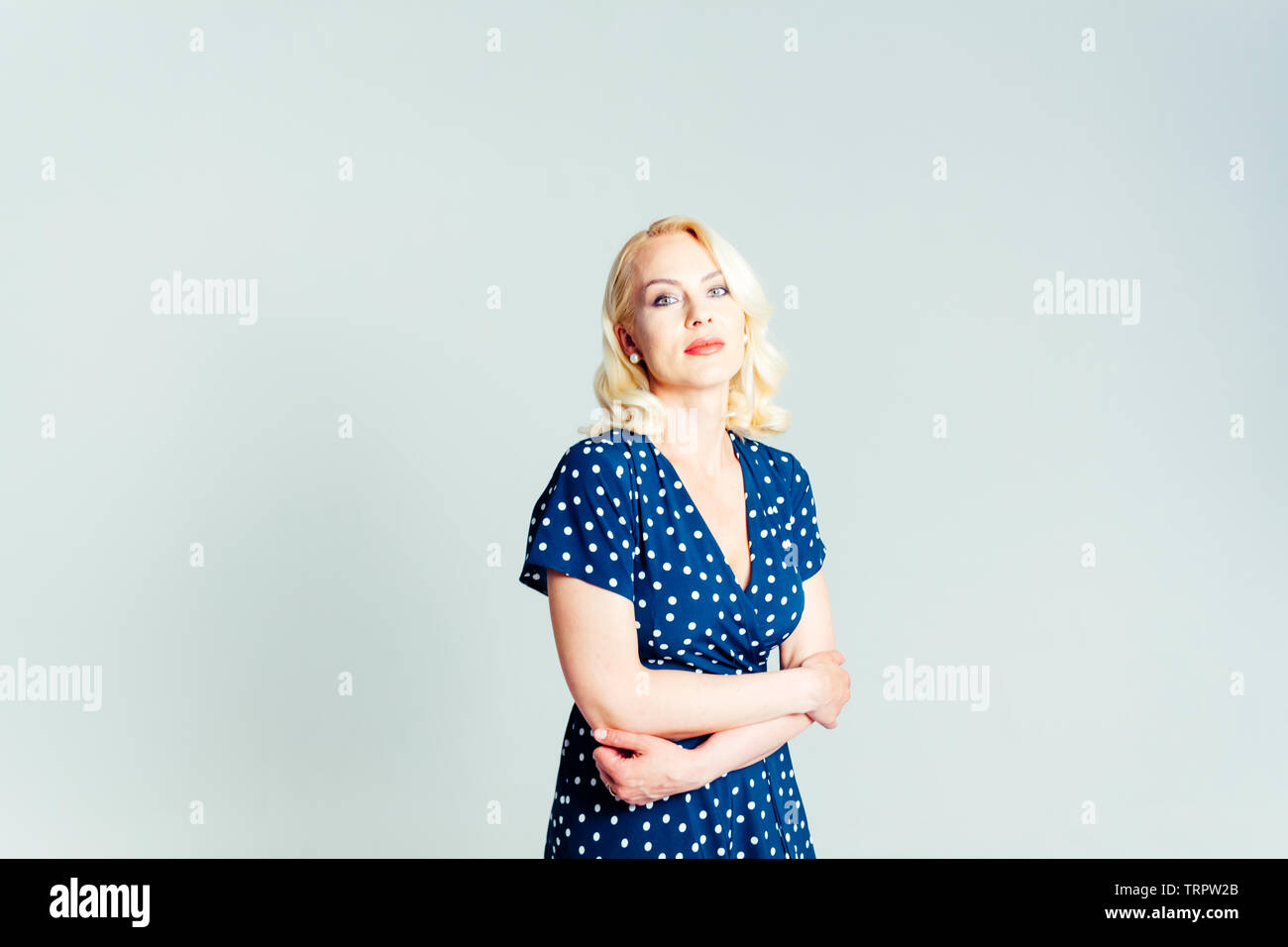 Studio portrait of beautiful blonde woman in a dark blue dress against white plain background Stock Photo