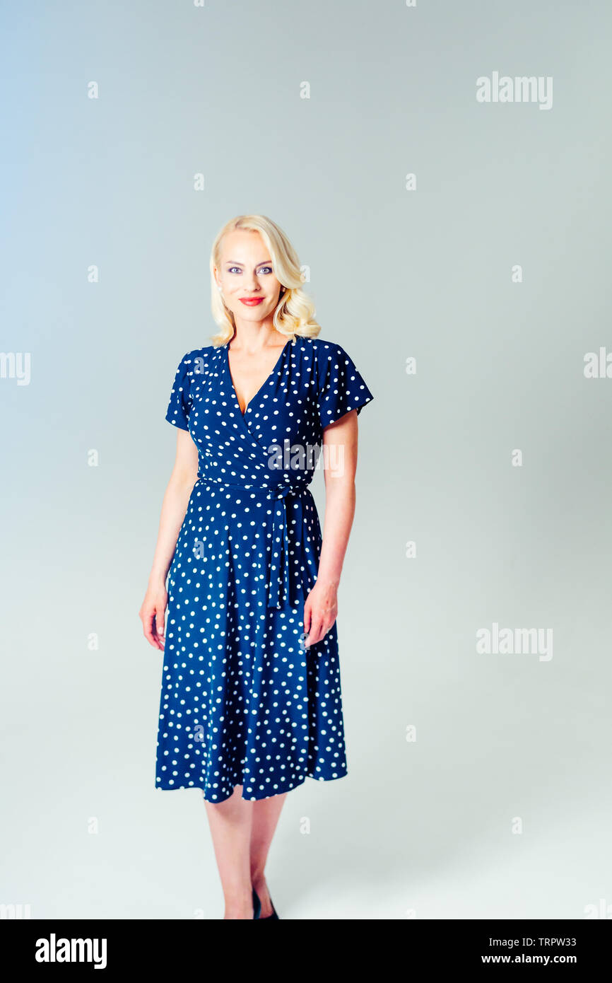 Studio portrait of beautiful blonde woman in a dark blue dress against ...