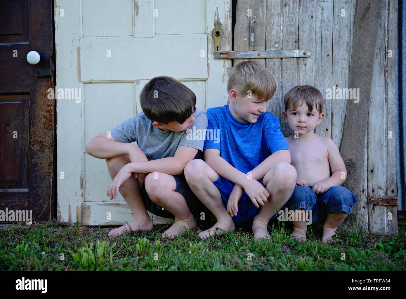 three boys sit by old wooden weathered doors Stock Photo
