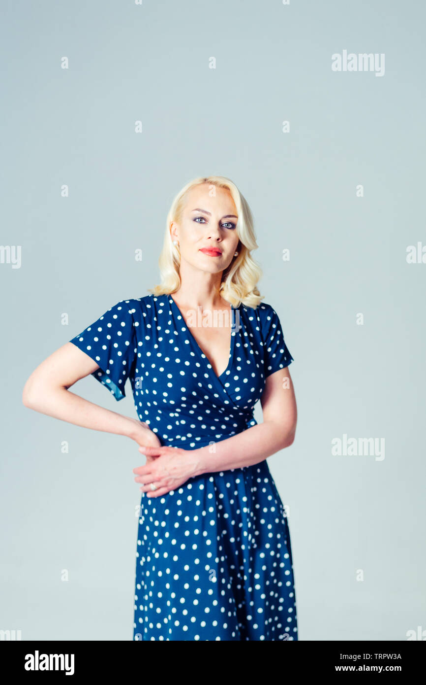 Studio portrait of beautiful blonde woman in a dark blue dress against ...