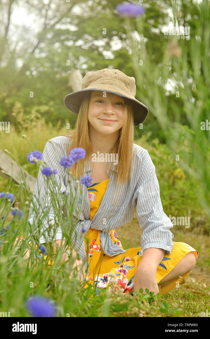 teenage girl portrait wearing a hat and sitting near bachelor button flowers on a farm Stock Photo