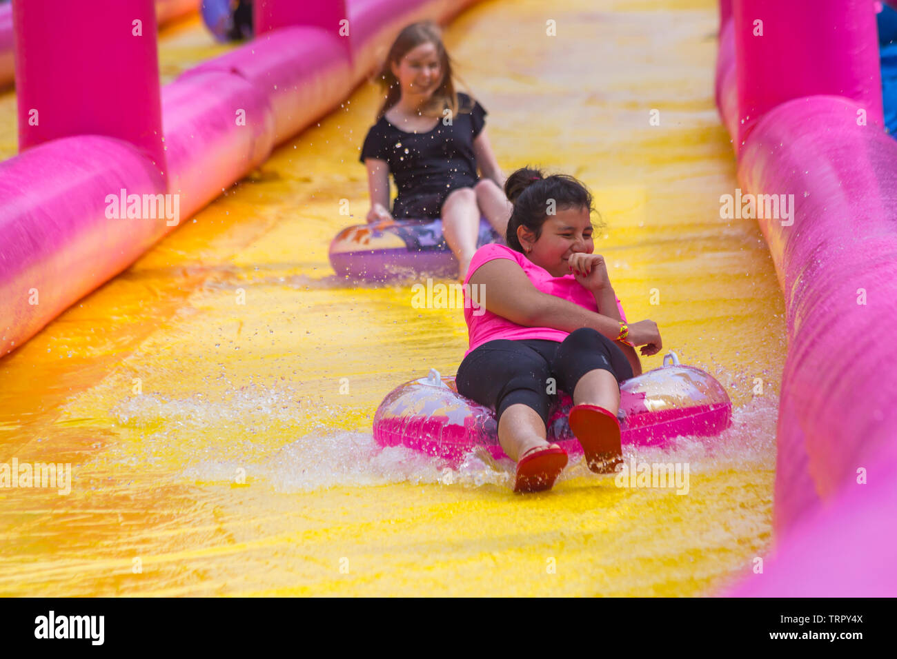 Girls sitting on inflatable rings having fun on giant waterslide, water slide, at Bournemouth, Dorset UK in June Stock Photo