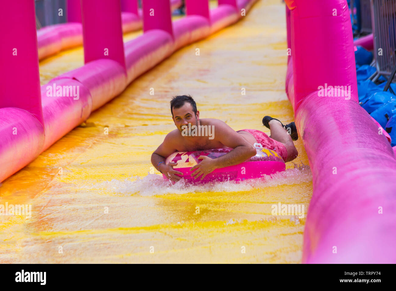 Man on inflatable ring having fun on giant waterslide, water slide, at Bournemouth, Dorset UK in June Stock Photo