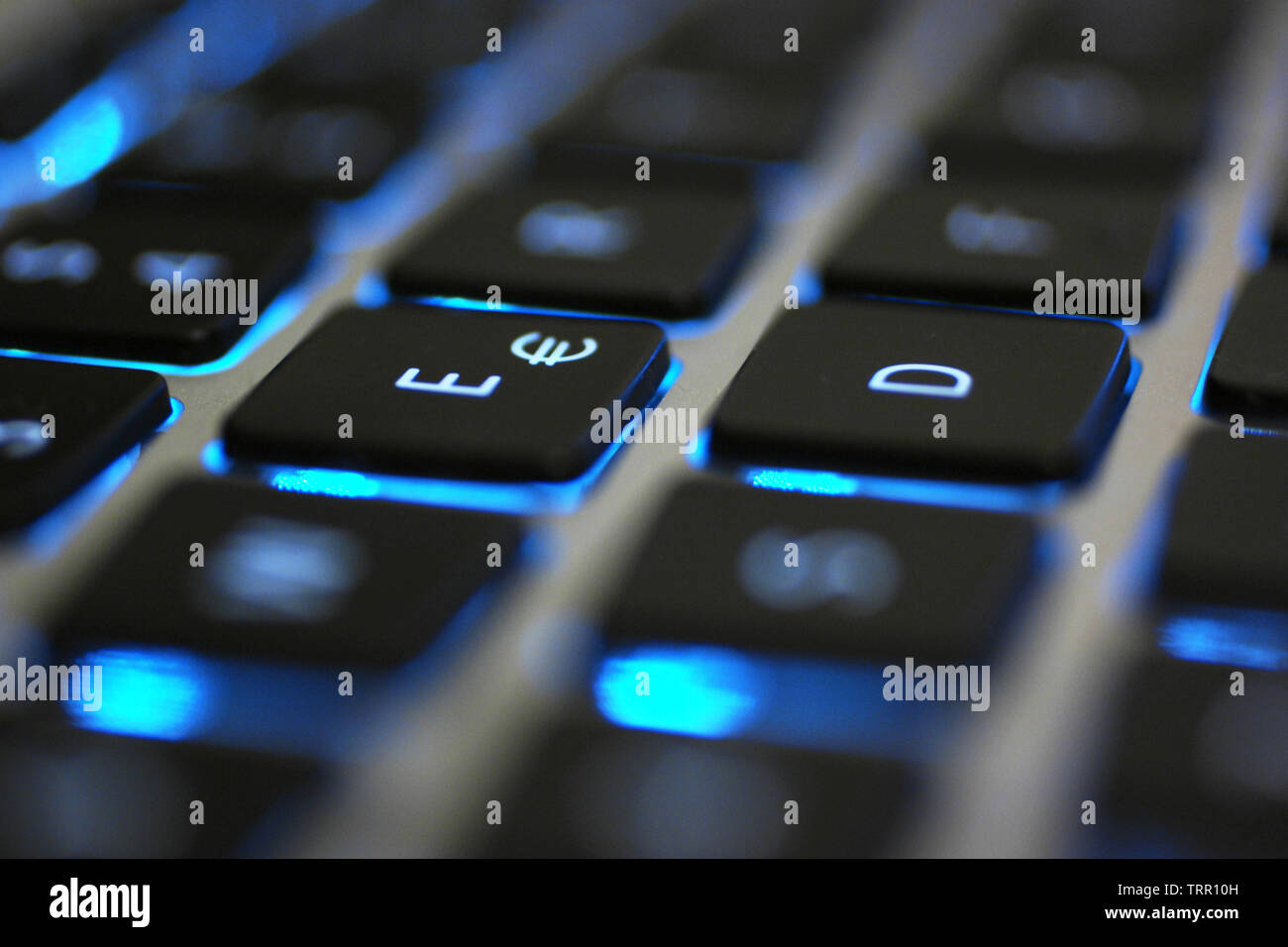 Laptop keyboard with blue backlight. Buttons closeup showing black details, white letters and silver body. Stock Photo