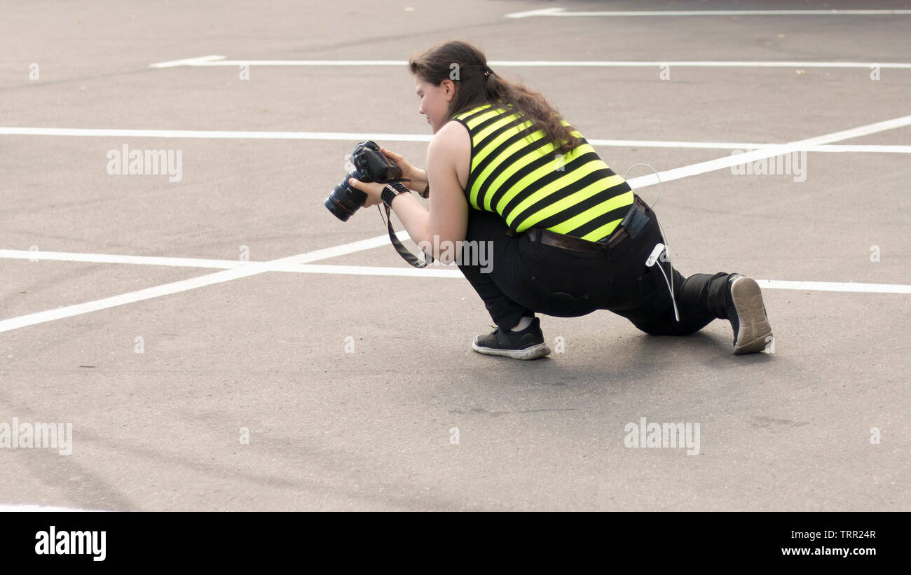 A female photographer with DSLR camera is shooting in the parking lot. Moscow - June 1, 2019. Hidden photographing, paparazzi concept. 16:9 image Stock Photo
