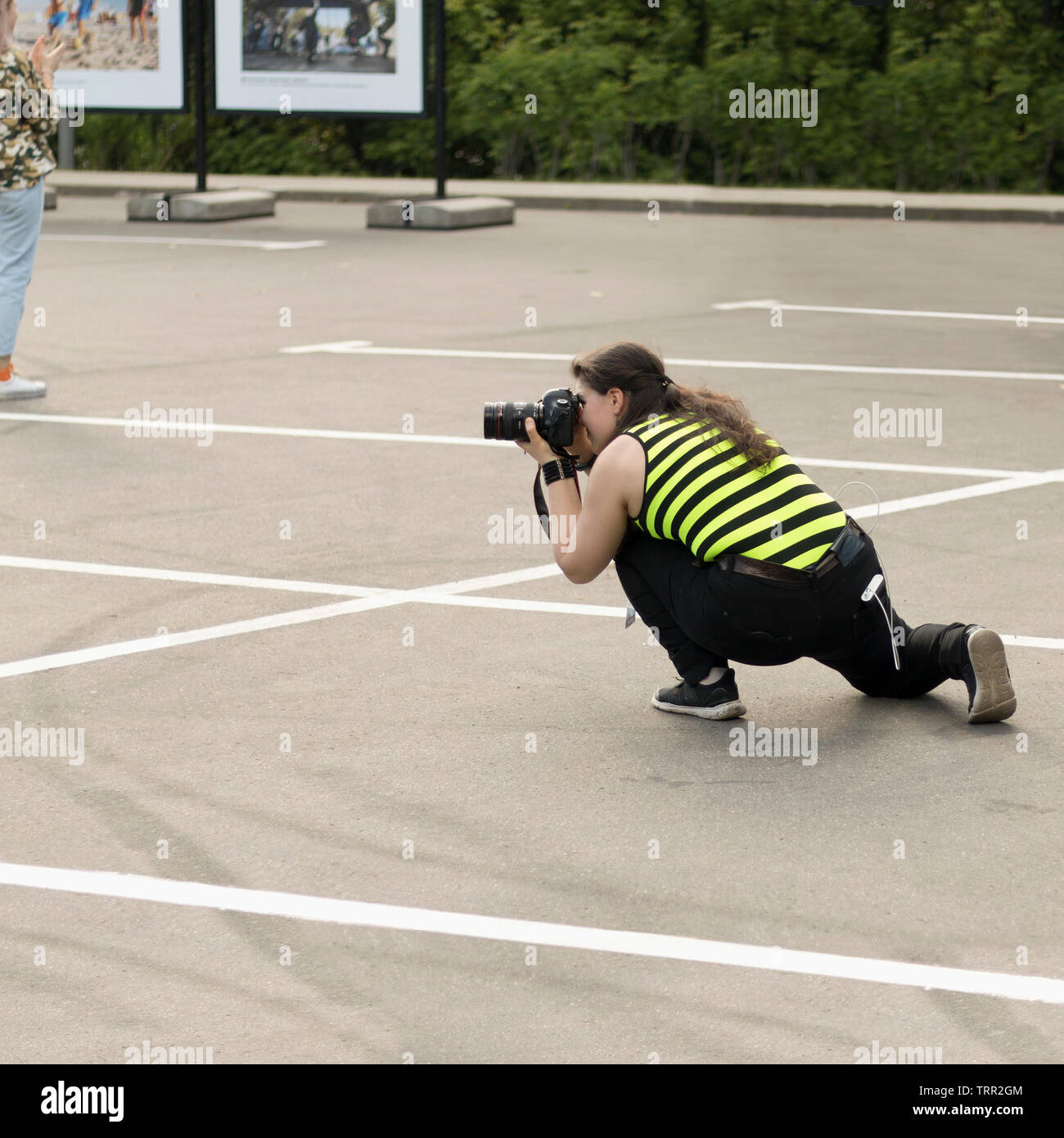 A female photographer with DSLR camera is secretly taking pictures of someone in exhibition outdoors. Moscow - June 1, 2019. Hidden photographing, pap Stock Photo