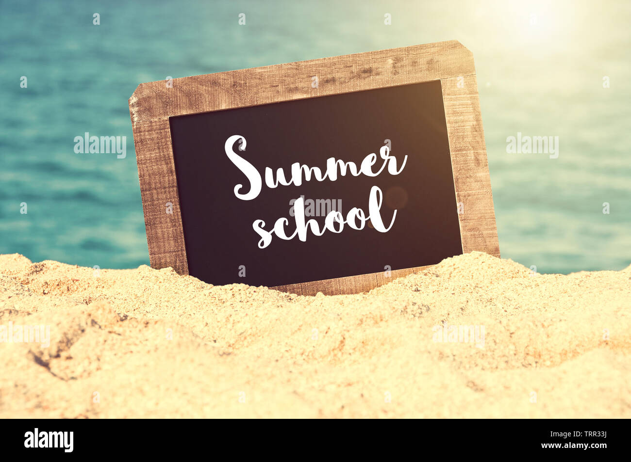 Summer school written on a vintage chalkboard in the sand of a beach ...