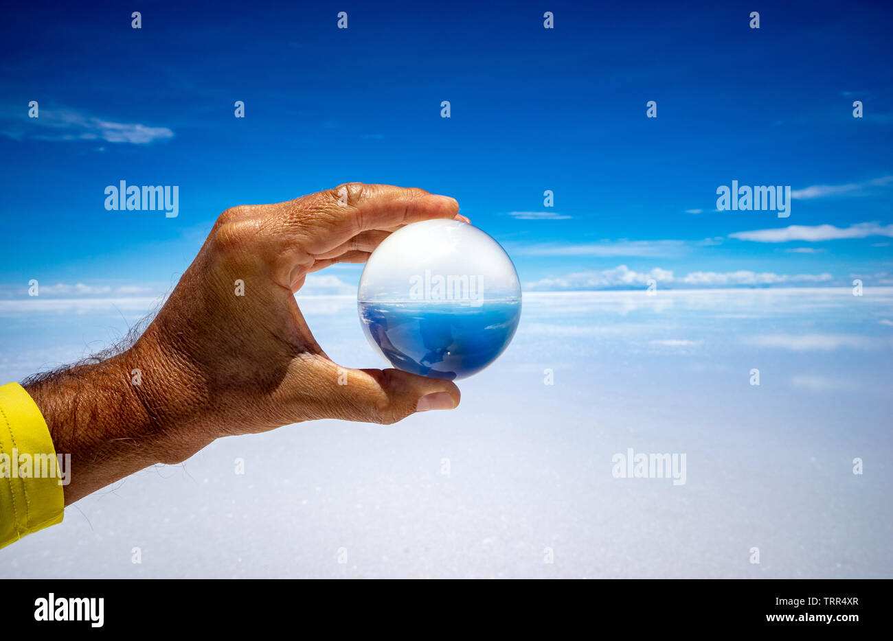Hand holding a crystal ball in front of a wide and sunny salt desert Stock Photo
