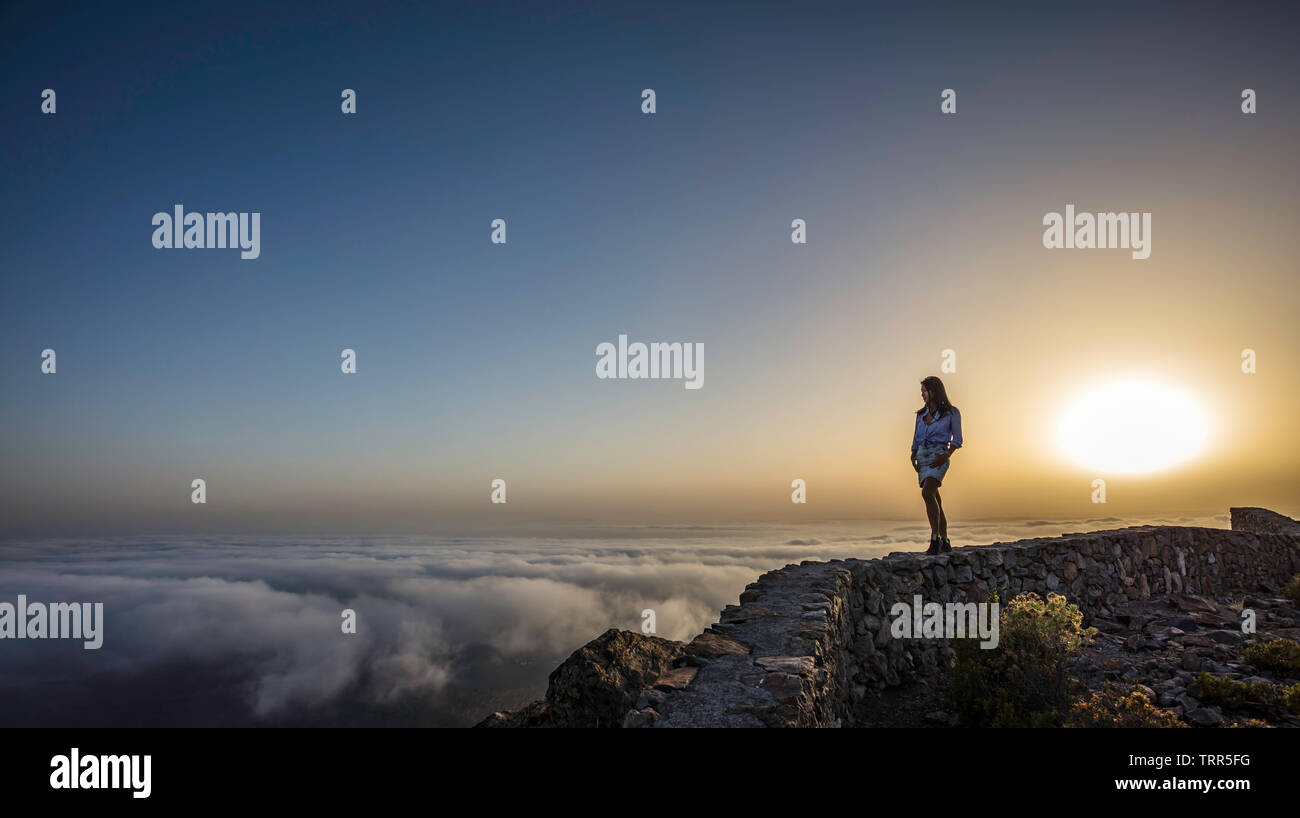 a woman on top of a mountain above the clouds during sunset Stock Photo
