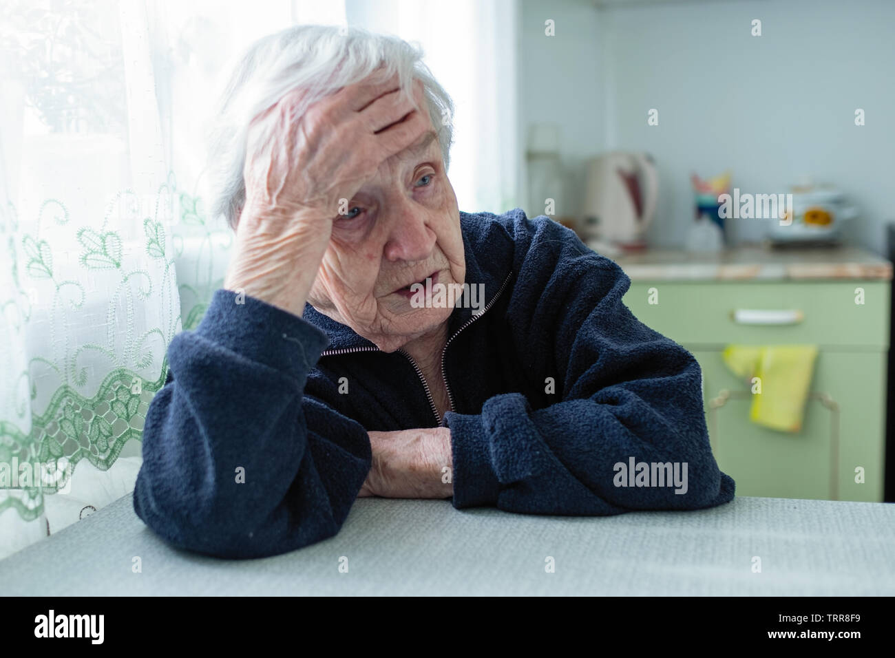 Frustrated gray-haired old woman sitting at home at the table. Stock Photo