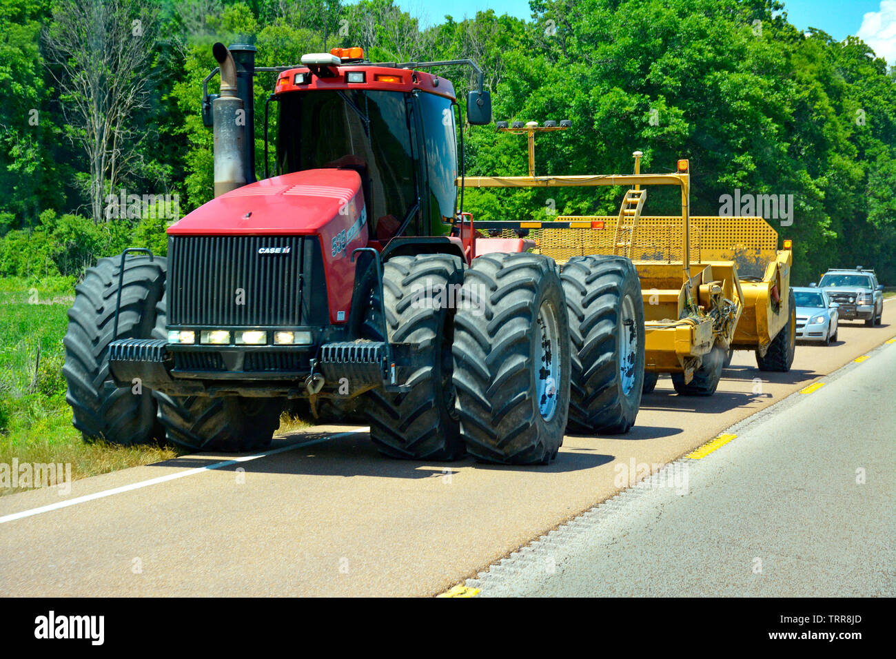 A huge, modern, farm tractor, a definite wideload, is holding up traffic as it travels down a rural highway in Northwestern Mississippi Stock Photo