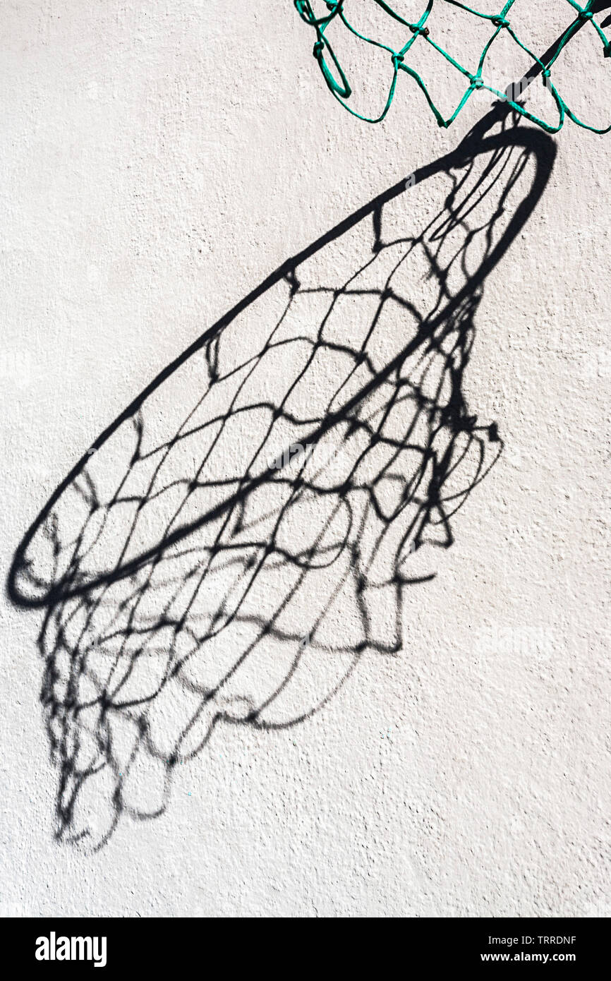 Abstract view of a hoop and net casting a large distorted shadow on a wall. Stock Photo