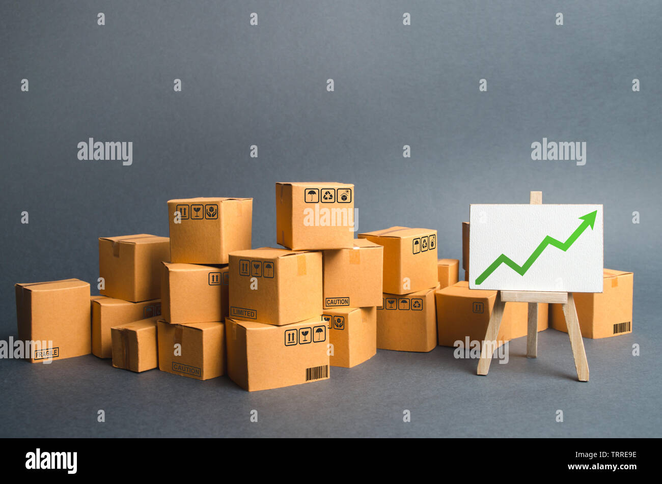 Lots of cardboard boxes and a stand with a green up arrow. rate growth of production of goods and products, increasing economic indicators. Increasing Stock Photo