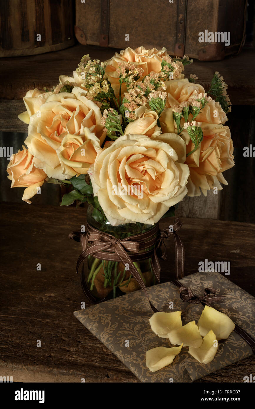 Natural window light on a small bouquet of Valencia roses and Statice. Photographed on a rustic wooden bench. Stock Photo